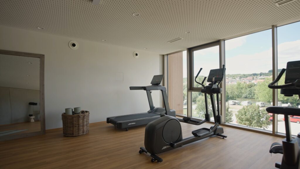 Imagefilm-Dreh Fitnessstudio-Interior Laufband-und-Crosstrainer Panorama-Fenster Tageslicht-Look Holzfußboden Spiegel-Detail Ruhe-Atmosphäre Corporate-Location Gesundheitsbenefit-Recruiting