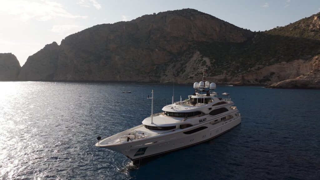 drohnenaufnahme-superyacht mittelmeer-bucht felsen-küste blaues-wasser goldenes-gegenlicht imagefilm-dreh yachtfilm-produktion produktvideo-yachtbranche cinematic-aufnahme maritim-location