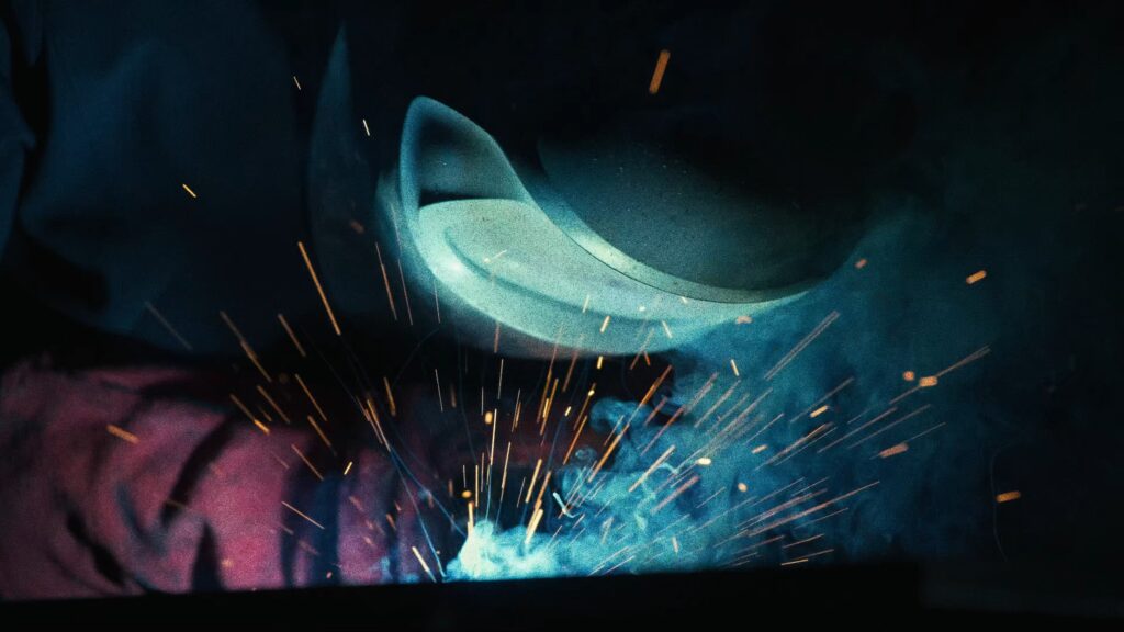 industrie-umgebung schweiß-prozess funkenflug nah-aufnahme metall-bearbeitung produktions-halle imagefilm-dreh b-roll werkstatt-atmosphäre sicherheits-helm low-key-licht rauch-effekte
