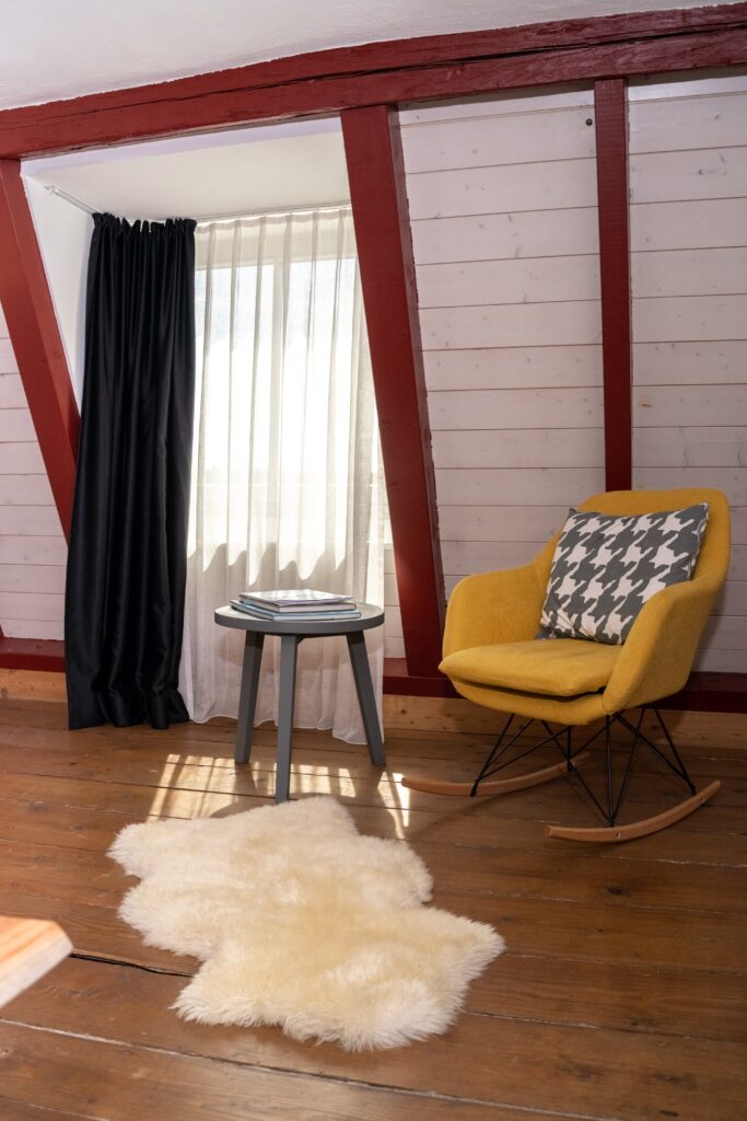 Interview-Setup Innenraum-Location Fenster-Licht Wohnliches-Set Gelber-Schaukelstuhl Beistell-Tisch Fell-Teppich Holz-Boden Vorhang-Look Schatten-Struktur Imagefilm-Dreh Corporate-Interview Recruiting-Video Set-Design