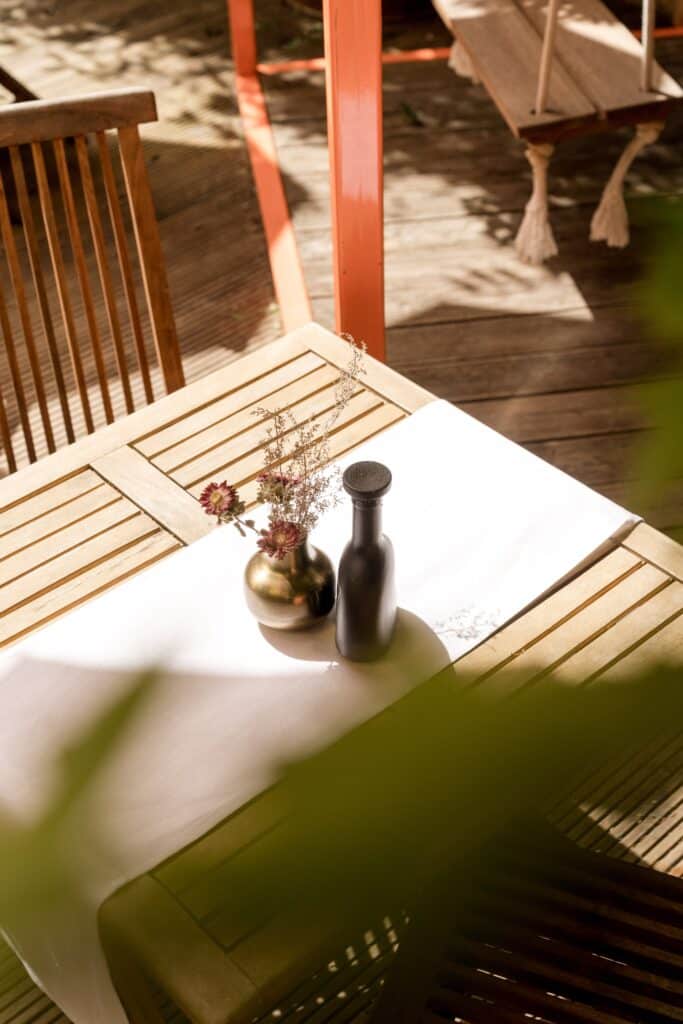 Produktvideo-Tabletop-Setup Outdoor-Terrasse Holztisch-Dekoration Vase-und-Flasche Natürliches-Seitlicht Cinematic-Schatten Gastronomie-Location Detail-Aufnahme