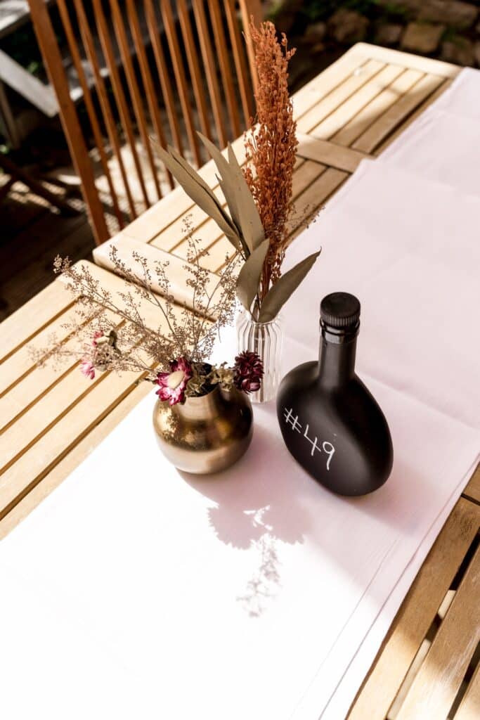 Produktvideo-Tabletop-Dreh Detailaufnahme-Still-Life Markeninszenierung-Requisiten Holztisch-Setting Deko-Setup Schwarze-Flasche-Prop Trockenblumen-Arrangement Tageslicht-Look Minimalistisches-Setdesign Nahaufnahme-Ästhetik