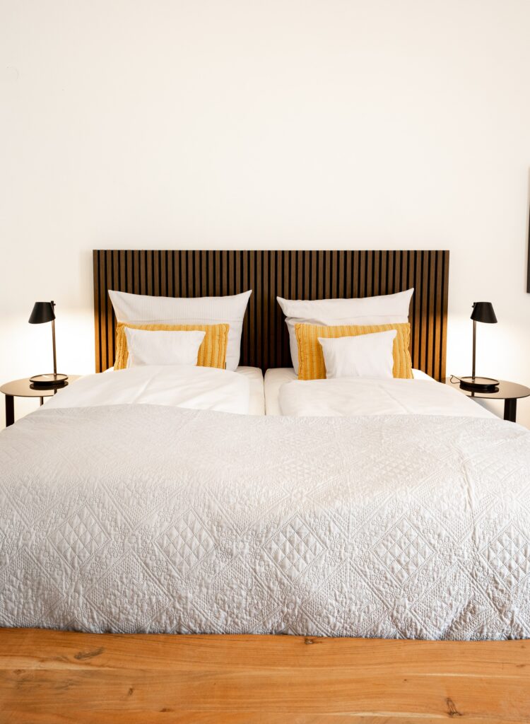 Interior-Aufnahme Hotelzimmer-Set Moderne-Ästhetik Symmetrische-Komposition Doppelbett-Holz-Kopfteil Weiße-Bettwäsche Gelbe-Kissen Nachttisch-Lampen Lifestyle-Produktvideo-Location Hospitality-Imagefilm-Location Location-Scouting