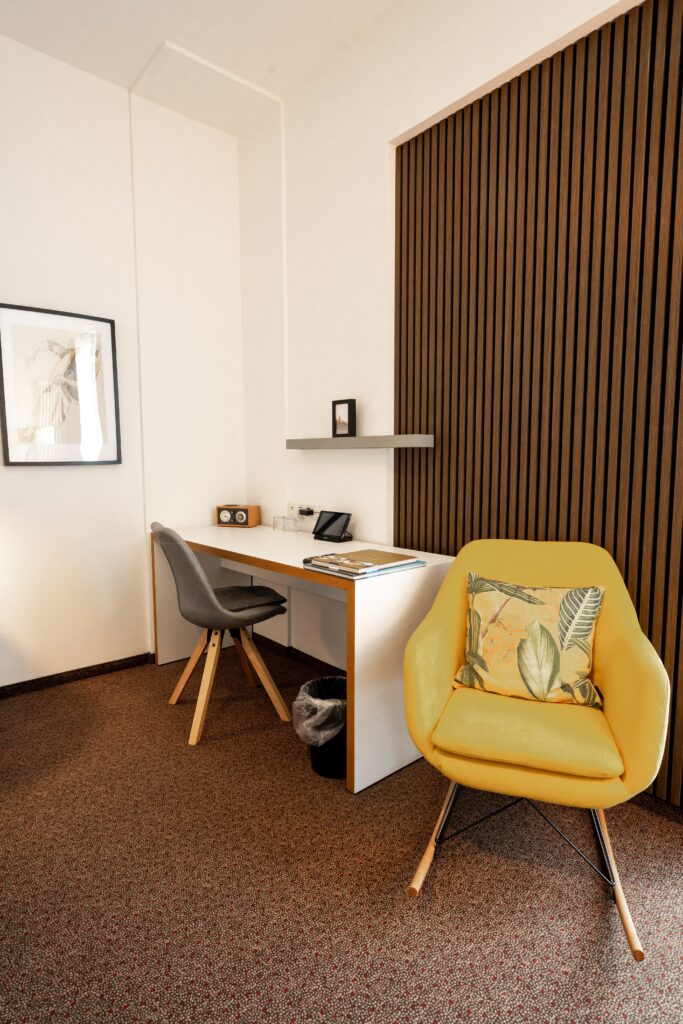 Imagefilm-Dreh, Interview-Setup, moderne-Büroszene, minimalistischer-Arbeitsplatz, Schreibtisch-mit-Stuhl, gelber-Designsessel, Holzlamellen-Wand, Corporate-Atmosphäre, B-Roll-Setdesign