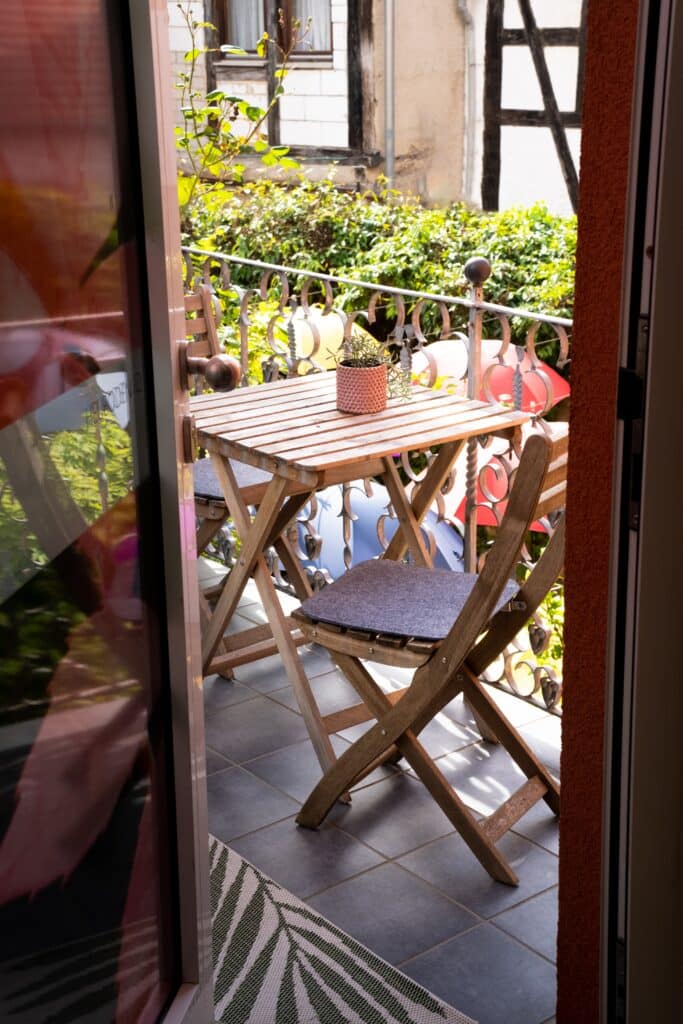 imagefilm-location-balkon, b-roll-terrasse, detailaufnahme-holztisch-stühle, pflanzen-dekor, tageslicht-aufnahme, urbanes-wohnambiente, schmiedeeisen-geländer, gemütliche-stimmung