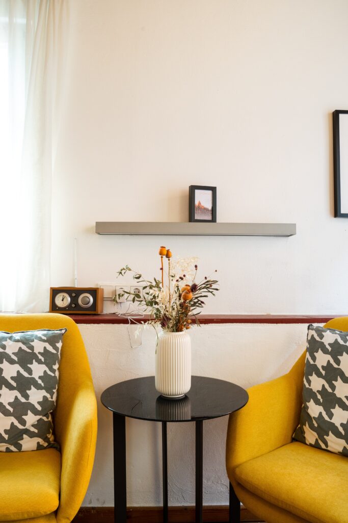 interview-setup, wohnliche-kulisse, gelbe-sessel, runder-beistelltisch, vase-mit-trockenblumen, retro-radio, natürliches-fensterlicht, minimalistisches-setdesign, b-roll-location