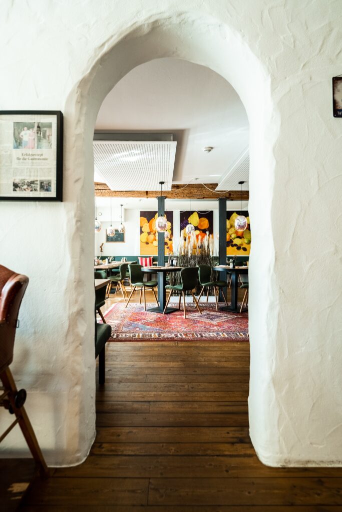 Restaurant-Interior, Gastronomie-Location, Imagefilm-Dreh, Ambiente-Aufnahme, Weitwinkel-Perspektive, Rundbogen-Durchgang, Holzboden, Orientteppich, Pendelleuchten, Bunte-Wandkunst, Location-Scouting, Gastro-Video