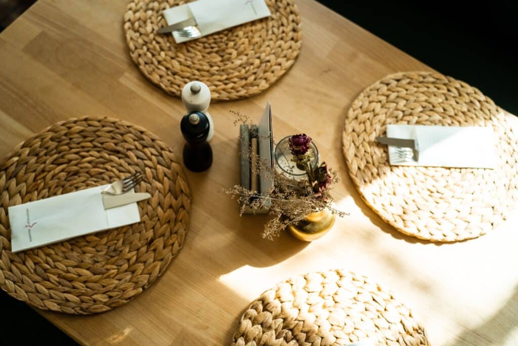 Produktvideo-Gastronomie, Imagefilm-Restaurant, Tabletop-Setup, Detailaufnahme-Holztisch, Geflochtene-Platzsets, Servietten-und-Besteck, Salz-und-Pfeffer-Mühlen, Trockenblumen-Deko, Natürliches-Fensterlicht