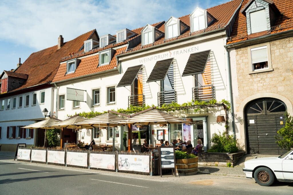 Gastronomie-Imagefilm, Weinbar-Terrasse, Restaurant-Außenbereich, Altstadt-Fassade, Sonnenschirm-Setup, Tageslicht-Aufnahme, Straßen-Setting, Gäste-Atmosphäre, Location-Scouting, Außenaufnahme-Setting, Tourismus-Marketing, Regional-Branding