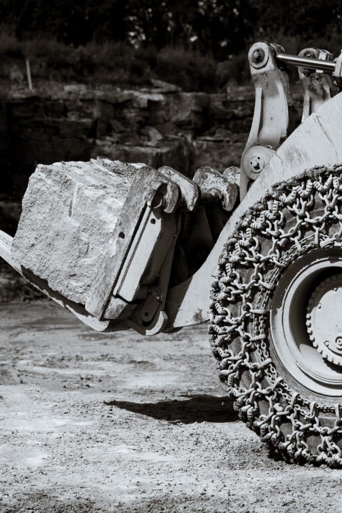 Industrieumgebung-Steinbruch Radlader-Baumaschine Schwerlast-Felsblock Schaufel-Detailaufnahme Reifenketten-Naheinstellung Imagefilm-Dreh-Industrie Produktvideo-Baumaschinen Schwarzweiß-Look Staubige-Atmosphäre