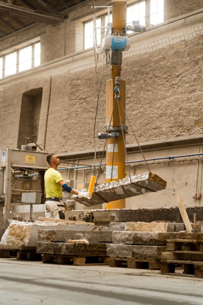 industrie-umgebung, stein-bearbeitung, kran-anlage, schwerlast-hebe-technik, werkstück-umladen, mitarbeiter-mit-fernbedienung, produktions-prozess, fabrik-halle, b2b-imagefilm, recruiting-video, produkt-video, industrie-aufnahme, sicherheits-ausrüstung