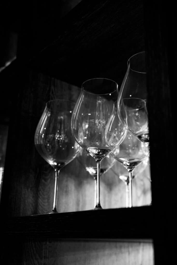Produktvideo-Gastronomie, Weinglas-Nahaufnahme, Schwarzweiß-Look, Low-Key-Licht, Regal-Detail, Bokeh-Reflexe, Imagefilm-Hotellerie, Premium-Ästhetik