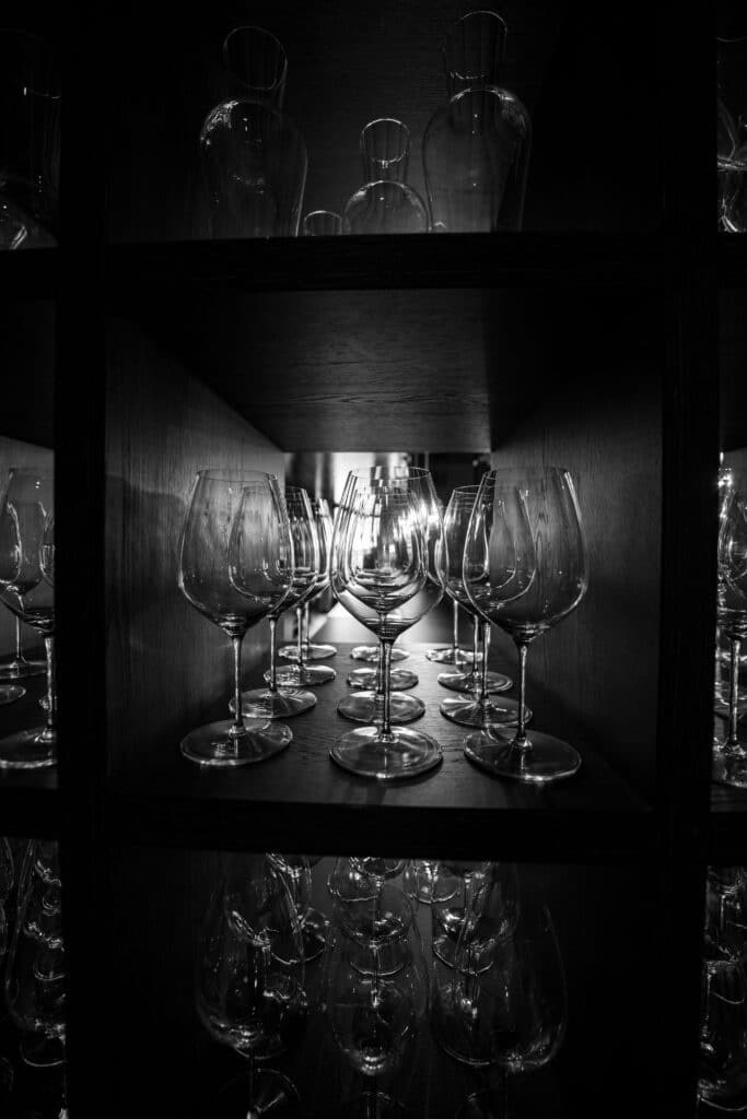 produktvideo-weingläser, gastronomie-imagefilm, detailaufnahme-glasregal, low-key-lichtsetup, spiegelungen-glas, b-roll-barinterieur, schwarzweiß-look, makro-perspektive, premium-branding, cineastische-stimmung
