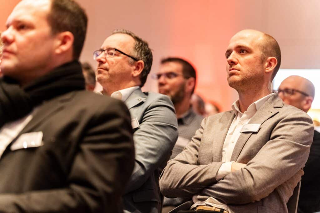 Business-Konferenz, Eventfilm-Dreh, Messefilm-Szene, Konferenz-Publikum, Corporate-Event, Publikums-Nahaufnahme, Warmlicht-Stimmung, B2B-Kommunikation