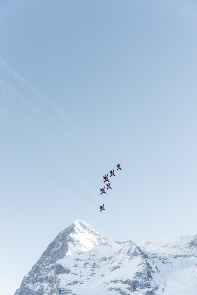 cinematische-luftaufnahme formationsflug-kunstflugjets über-schneebedeckten-alpengipfeln klarer-himmel action-sequenz imagefilm-dreh highspeed-ästhetik
