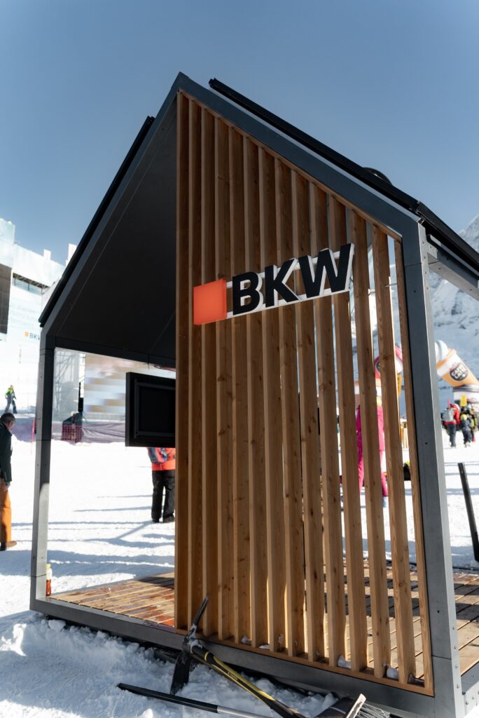 Messefilm-Outdoor-Event, Marken-Pavillon, Holz-Architektur, Winter-Schneekulisse, Alpen-Location, BKW-Branding, Produktpräsentation-Stand, Event-Dokumentation, Imagefilm-Szene, Drohnenaufnahme-Potenzial