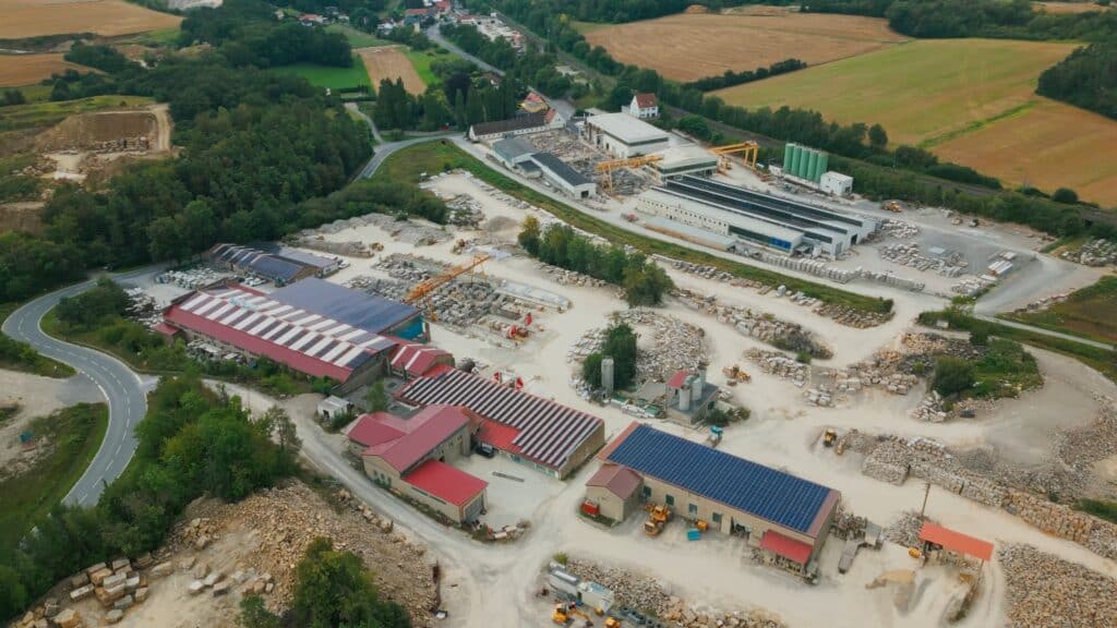 drohnenaufnahme-industrieumgebung steinbruch-natursteinwerk produktionshallen-mit-solarpaneelen krananlagen-und-baumaschinen lagerflächen-mit-steinblöcken logistik-und-werksinfrastruktur b2b-imagefilm-produktvideo