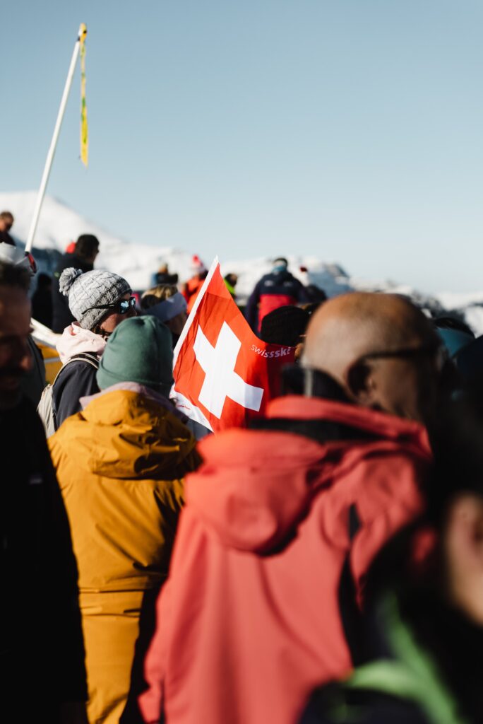Eventfilm-Produktion Outdoor-Event Wintersport-Szene Schweizer-Flagge Berg-Kulisse Menschen-Menge Imagefilm-Dreh On-Location-Dreh Reportage-Stil Available-Light
