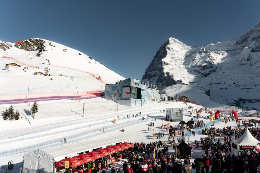 Eventfilm-Wintersport Skirennen-Alpenkulisse Weitwinkel-Aufnahme Zielbereich-mit-Zuschauern Sponsoren-Branding Großbildschirm-Live-Übertragung Schnee-Piste-mit-Absperrungen Outdoor-Imagefilm-Dreh