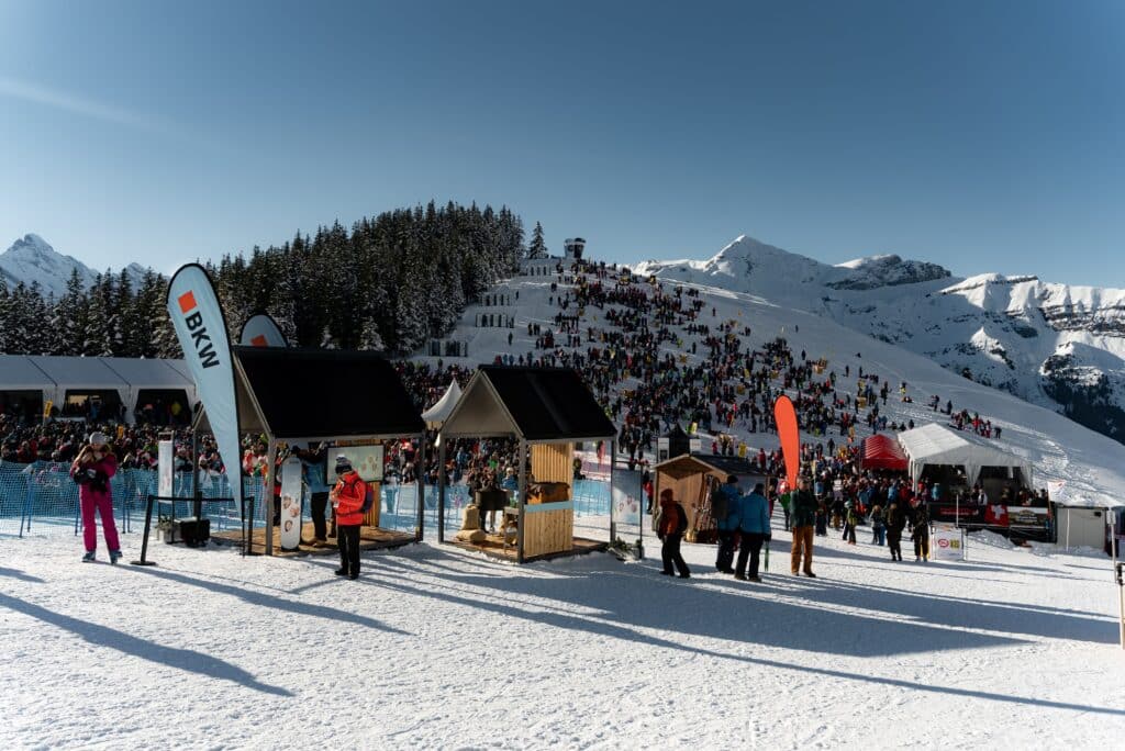 Eventfilm-Wintersport Alpen-Schnee Skipisten-Crowd Sponsoren-Flags Festival-Zelte Outdoor-Event Drohnenaufnahme-Potenzial Kamera-Setup-Reportage Markenpräsenz-Branding Wintersonne-Berge