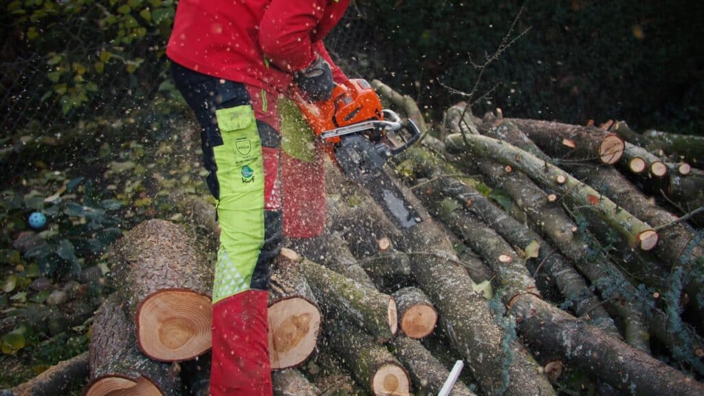 Kettensägen-Einsatz, Holzstämme-Zersägen, Baumpflege-Handwerk, Sicherheitskleidung-Nahaufnahme, Outdoor-Industrieumgebung, Imagefilm-Dreh