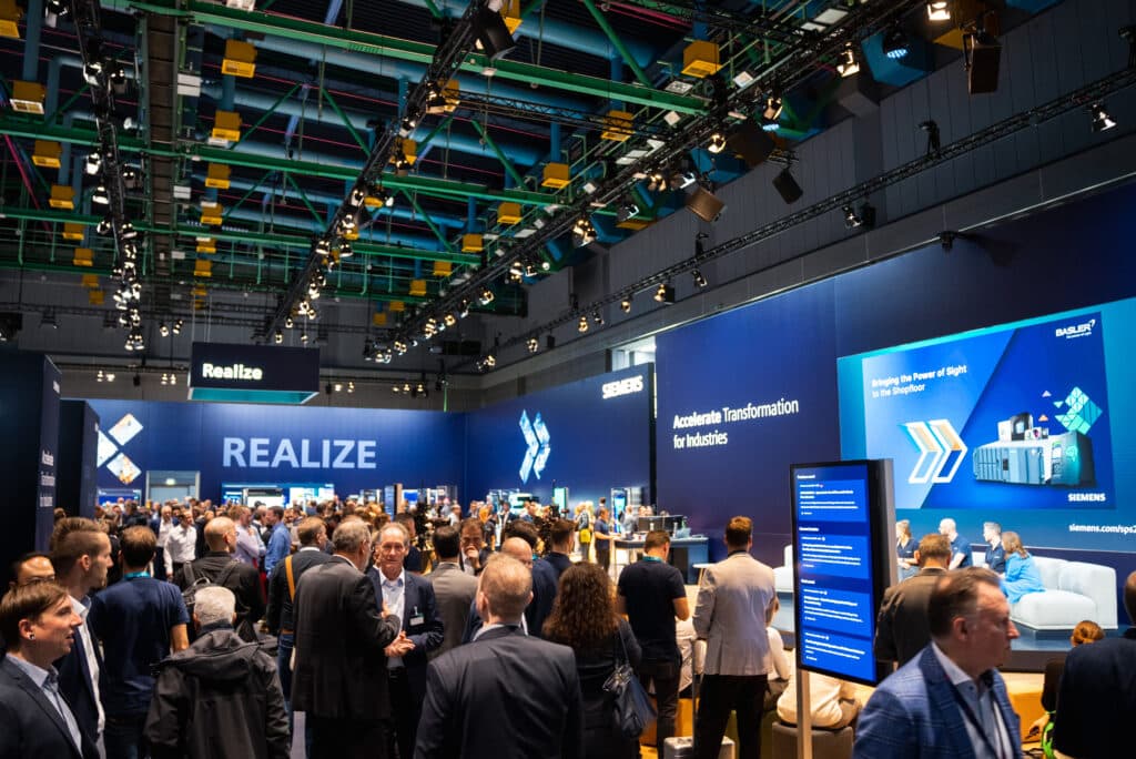 Messefilm-Produktion Technologiemesse-Industriehalle Messestand-Inszenierung LED-Wand-Präsentation Bühnen-Talk Live-Event-Atmosphäre B2B-Besucherandrang Licht-Rig-Bühnenbau Marken-Auftritt Event-Video-Dokumentation