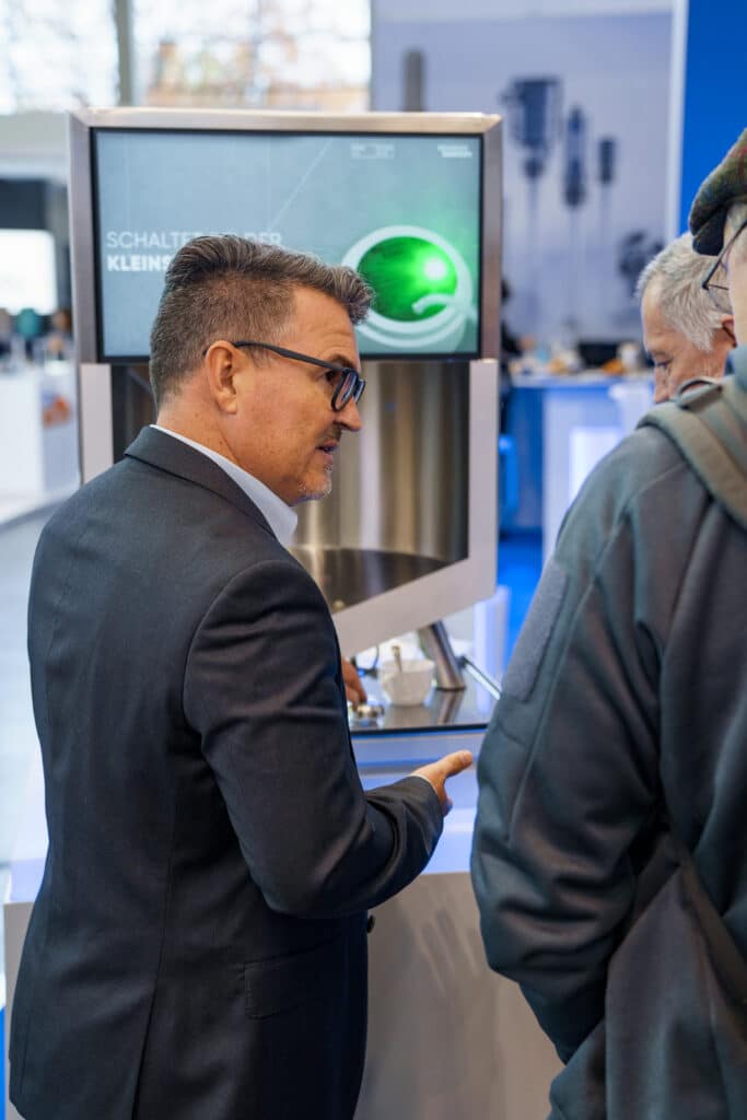 Messefilm-Szene Produktpräsentation-Industrie Messestand-Detail B2B-Event Technik-Demo Kunden-Interaktion Display-Monitor Business-Nahaufnahme Beratungs-Gespräch