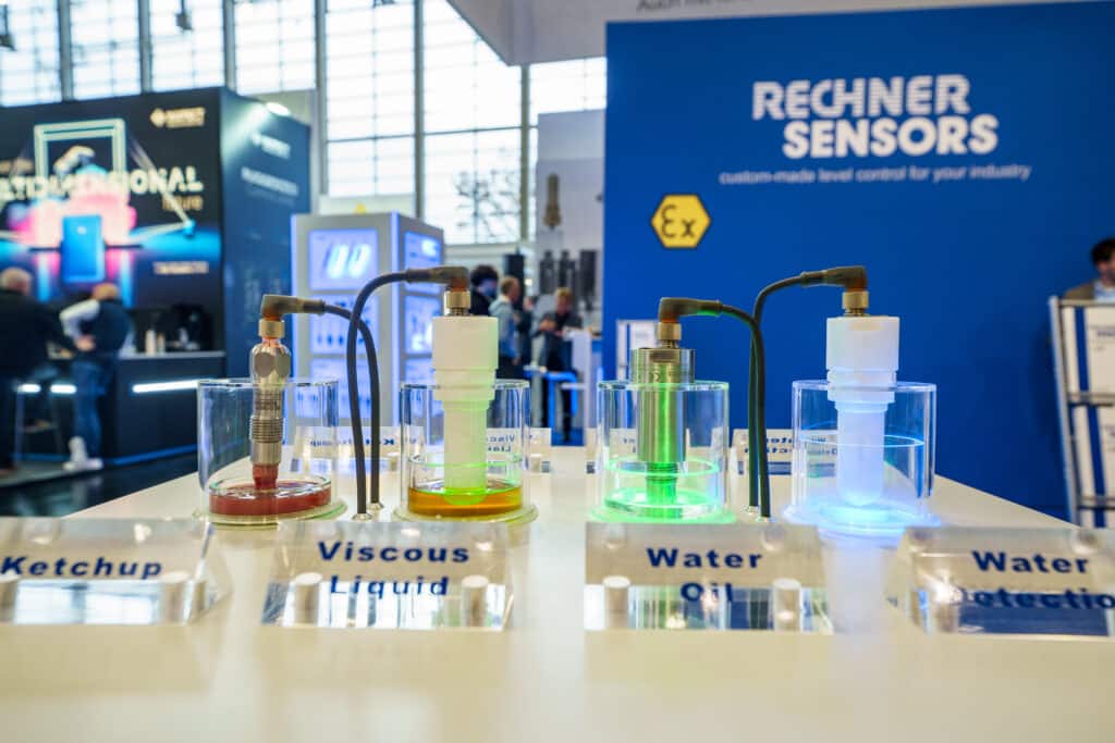 Messefilm-Produktvideo Industrieumgebung-Sensortechnik Füllstandssensor-Demonstration Flüssigkeitsmessung-Showcase Glaszylinder-Exponate LED-Beleuchtungs-Details Technik-Nahaufnahme Messestand-Branding B2B-Technologieaufnahme