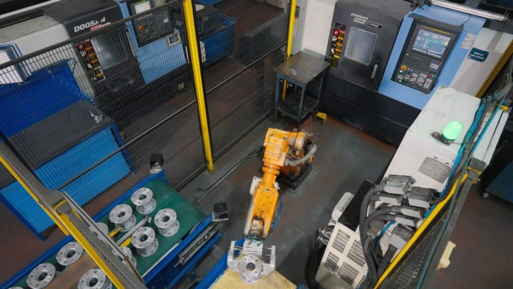 industrieumgebung-automatisierte-produktion-roboterarm-CNC-drehmaschine-metallbearbeitung-metallteile-förderband-sicherheitszaun-top-down-aufnahme-produktvideo